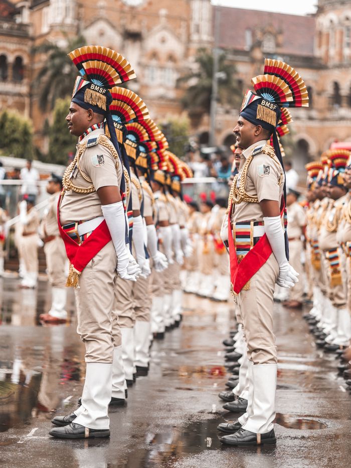 Colorful parade with guards in uniform standing before a historic building under cloudy skies.
